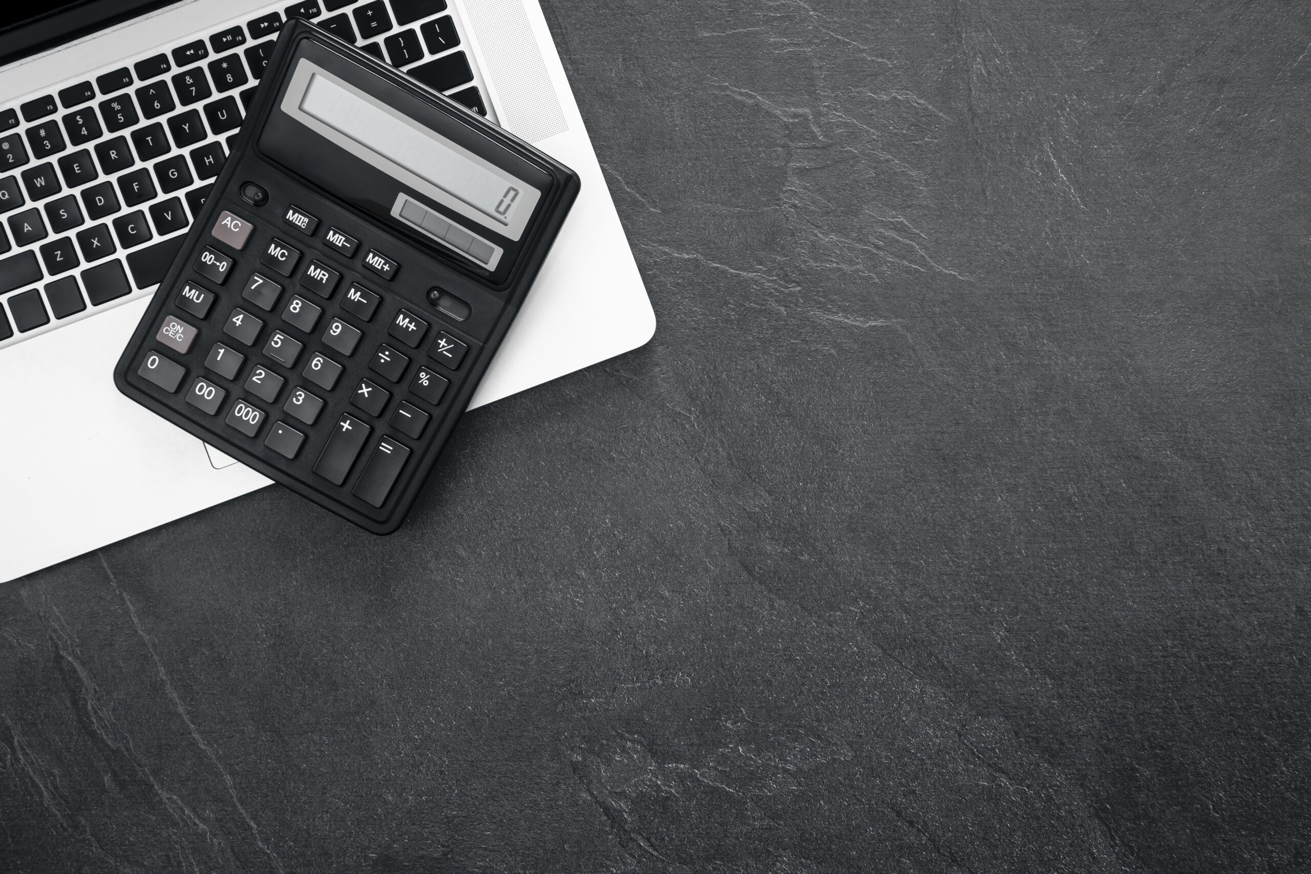 Calculator and laptop on a textured black background, top view.
